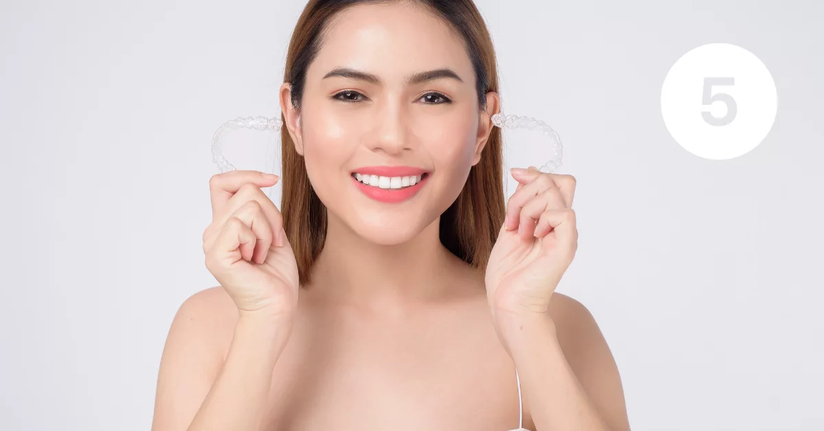 5 Woman smiling and holding up 2 Invisalign aligners.